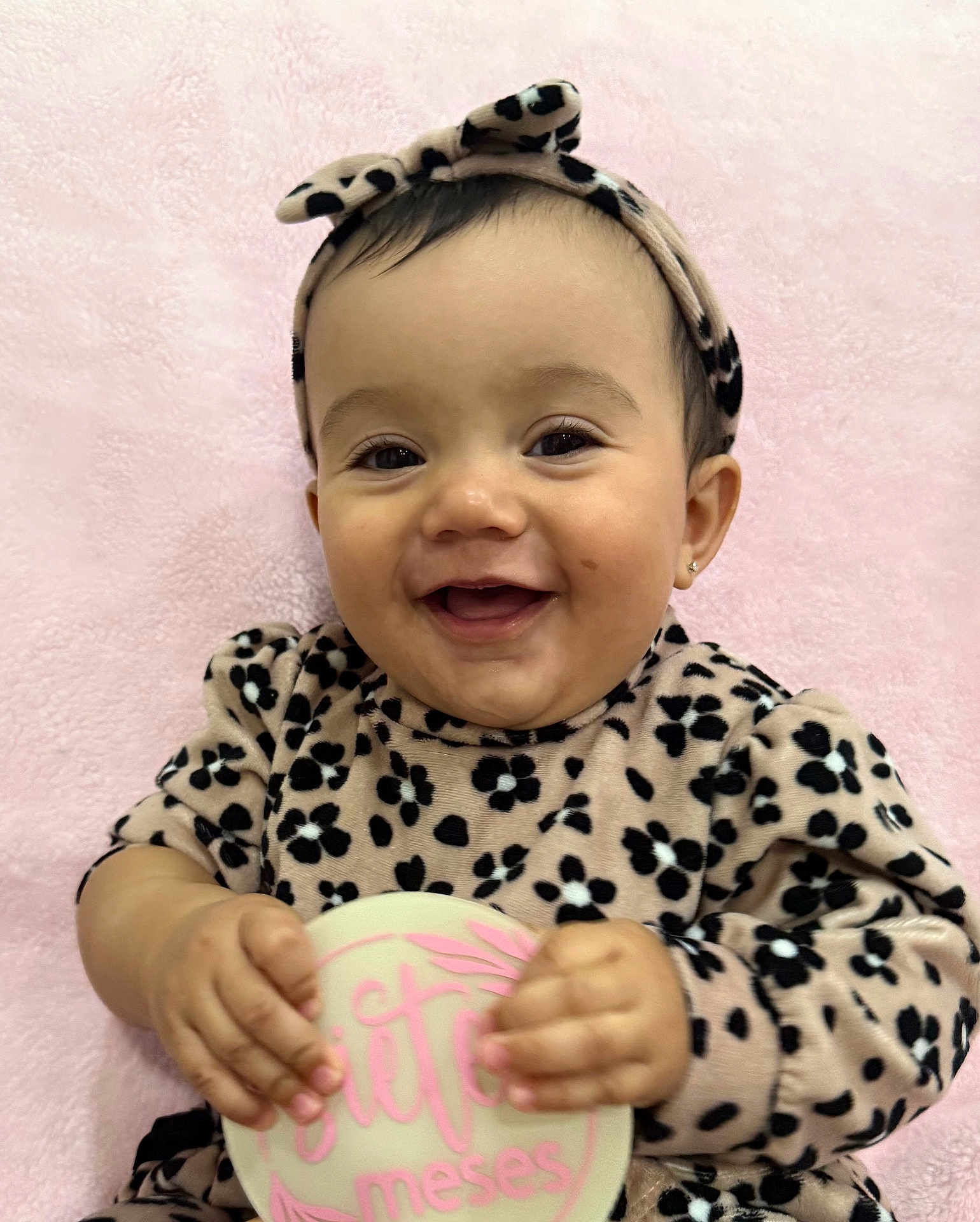 Liah joined the competition — help win amazing prizes! baby, infant, smiling, headband, bow, blanket, pink_background, leopard_print, outfit, holding_milestone, hands, face, eyes, mouth, earring, close_up, portrait, happy, soft_texture, cheeks