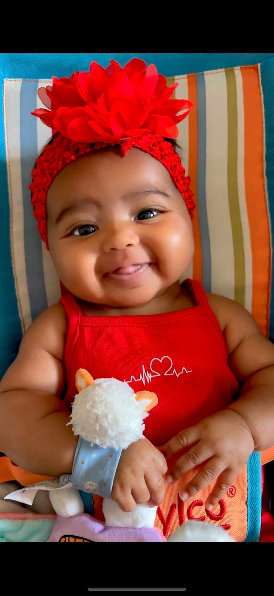 Dayana participe au concours pour gagner de l'argent avec cette photo : baby, smiling, red_headband, flower, toy, plush_toy, infant, cute, chubby_cheeks, colorful_background, striped_cushion, red_outfit, happy, portrait, child, hand, face, indoors, closeup, person