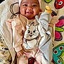 baby, smiling, pink_bow, headband, plush_toy, dumbo, cat_sweater, flower_pants, socks, blanket, cushion, indoor, cute, child, happy, portrait, infant, soft_toys, clothing, cozy