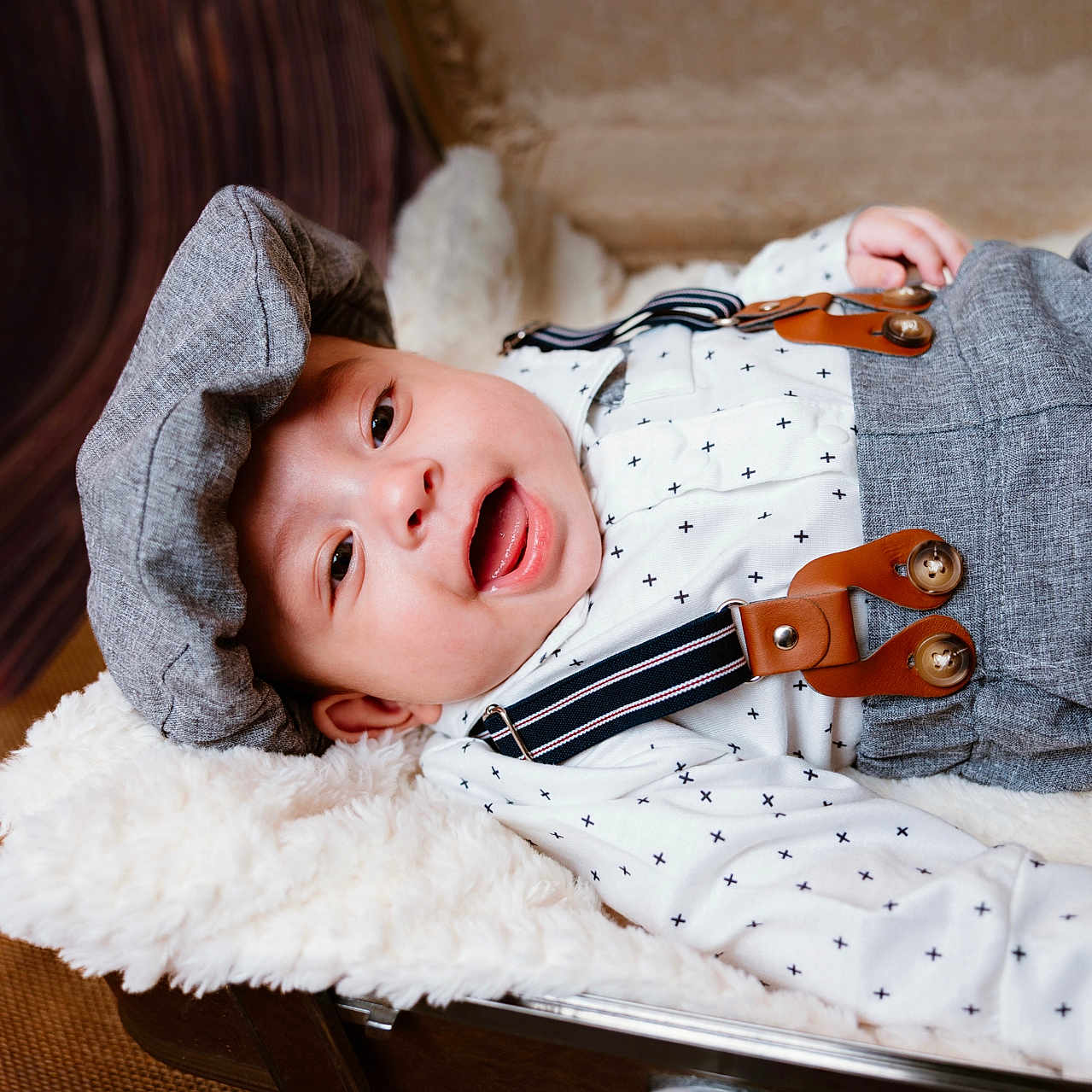 Ricardo joined the competition — help win amazing prizes! baby, infant, smile, face, cap, suspenders, clothing, white_shirt, patterned_shirt, blanket, fur_blanket, suitcase, wooden_floor, happy, cute, portrait, lying_down, indoors, child, young_baby
