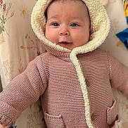 Hazel is registered to the contest to win money with this photo: baby, infant, knitted_jacket, hood, bear_ears, pink_clothing, cozy, cute, smile, face, child, soft_texture, buttoned_jacket, pocket, floral_background, lying_down, warm, indoors, portrait, happy