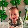 baby, balloons, celebration, chubby_cheeks, clover, cute, face, green_balloons, green_outfit, hands, indoor, infant, lying_down, onesie, portrait, shamrock, smiling, soft_lighting, st_patricks, tummy_time