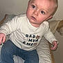 toddler, child, baby, jeans, socks, shirt, text_on_clothing, indoor, changing_table, cushion, wooden_frame, face, eyes, curious, sitting, blond_hair, long_sleeve, skin, person, young_child