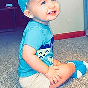 Emmett is registered to the contest to win money with this photo: toddler, child, blue_cap, blue_shirt, smiling, indoor, carpet, sitting, happy, cute, shorts, baby, young_child, casual_clothing, portrait, playful, face, headwear, feet, light