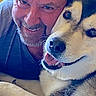 Balto is registered to the contest to win money with this photo: man, person, dog, pet, selfie, portrait, close_up, smiling, cuddling, companionship, friendship, black_and_white_dog, collar, whiskers, fur, face, eyes, nose, indoor, warm_lighting