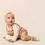 baby, infant, crawling, headband, bow, romper, floral_pattern, white_shoes, curious, wide_eyes, child, indoor, studio, soft_lighting, cream_background, cute, adorable, fashion, portrait, toddler
