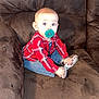 Zechariah is registered to the contest to win money with this photo: baby, child, pacifier, red_shirt, plaid, jeans, toy, couch, brown, furniture, indoor, sitting, person, infant, cute, wide_eyes, clothing, holding, young, home