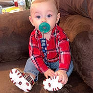 Zechariah is registered to the contest to win money with this photo: baby, pacifier, red_shirt, plaid, blue_jeans, sitting, couch, brown_furniture, indoor, flowers, vase, water_bottle, child, cute, footwear, shoes, home, portrait, infant, cozy