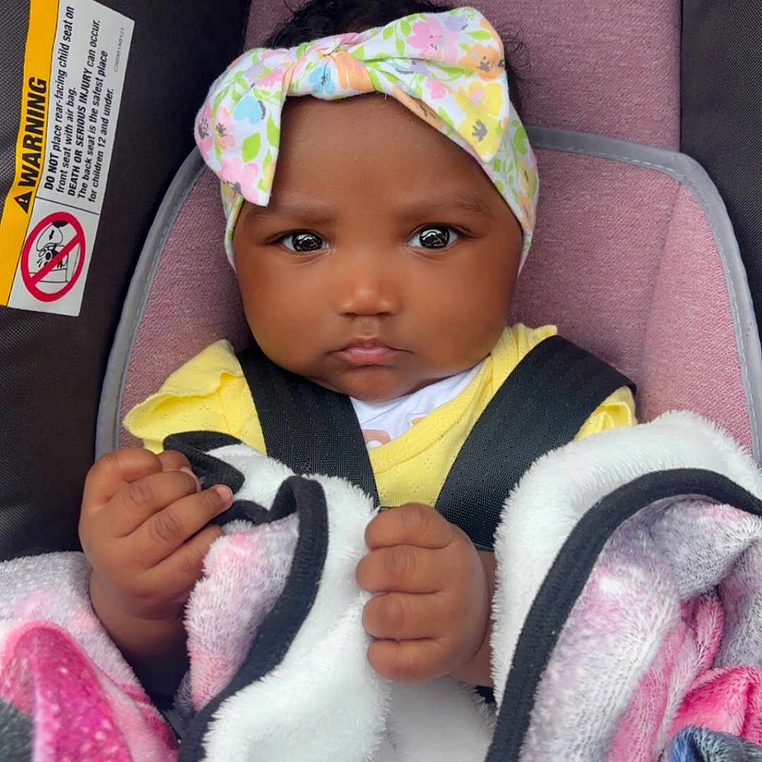 Quayla joined the competition — help win amazing prizes! baby, blanket, car_seat, child, closeup, clothing, colorful, cute, expression, face, hands, headband, indoor, infant, person, pink, portrait, sitting, straps, yellow