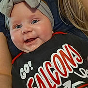 Natalee joined the competition — help win amazing prizes! baby, child, smiling, headband, bow, shirt, text, person, face, happy, cheer, sports, team_spirit, closeup, indoor, skin, hand, eyes, clothing, infant