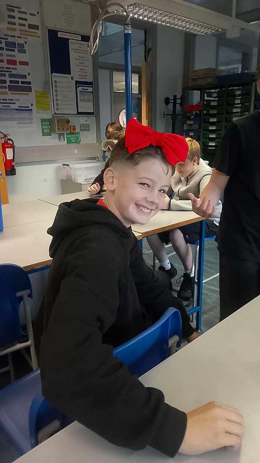 Crackwhore is registered to the contest to win money with this photo: child, smiling, red_bow, bow, hoodie, black_hoodie, classroom, desk, chair, student, school, classmates, shelf, notice_board, fire_extinguisher, fluorescent_light, indoor, sneakers, hand, portrait