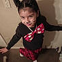 Delilah is registered to the contest to win money with this photo: child, girl, face_paint, cat_whiskers, hair_buns, bow_tie, red, black, plaid_pants, indoor, carpet, smile, playful, costume, cute, posing, person, fashion, happy, fun