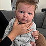 Albie joined the competition — help win amazing prizes! baby, infant, child, hand, couch, gray_couch, gray_clothing, indoor, person, face, blue_eyes, sitting, expression, adult_hand, ring, plaid_pants, home, soft_lighting, portrait, curly_hair