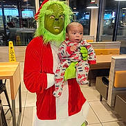 Lashawn is registered to the contest to win money with this photo: grinch_costume, baby, child, pajamas, fire_truck_pattern, person, restaurant, indoor, window, night, exit_sign, table, chair, booth_seating, floor_tile, wet_floor_sign, costume, holiday, green_face, red_clothing