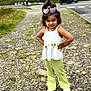 child, girl, outdoor, path, rocks, greenery, road, car, sunglasses, white_top, green_pants, standing, posing, hair_tied, confident, footwear, nature, portrait, casual_clothing, daylight