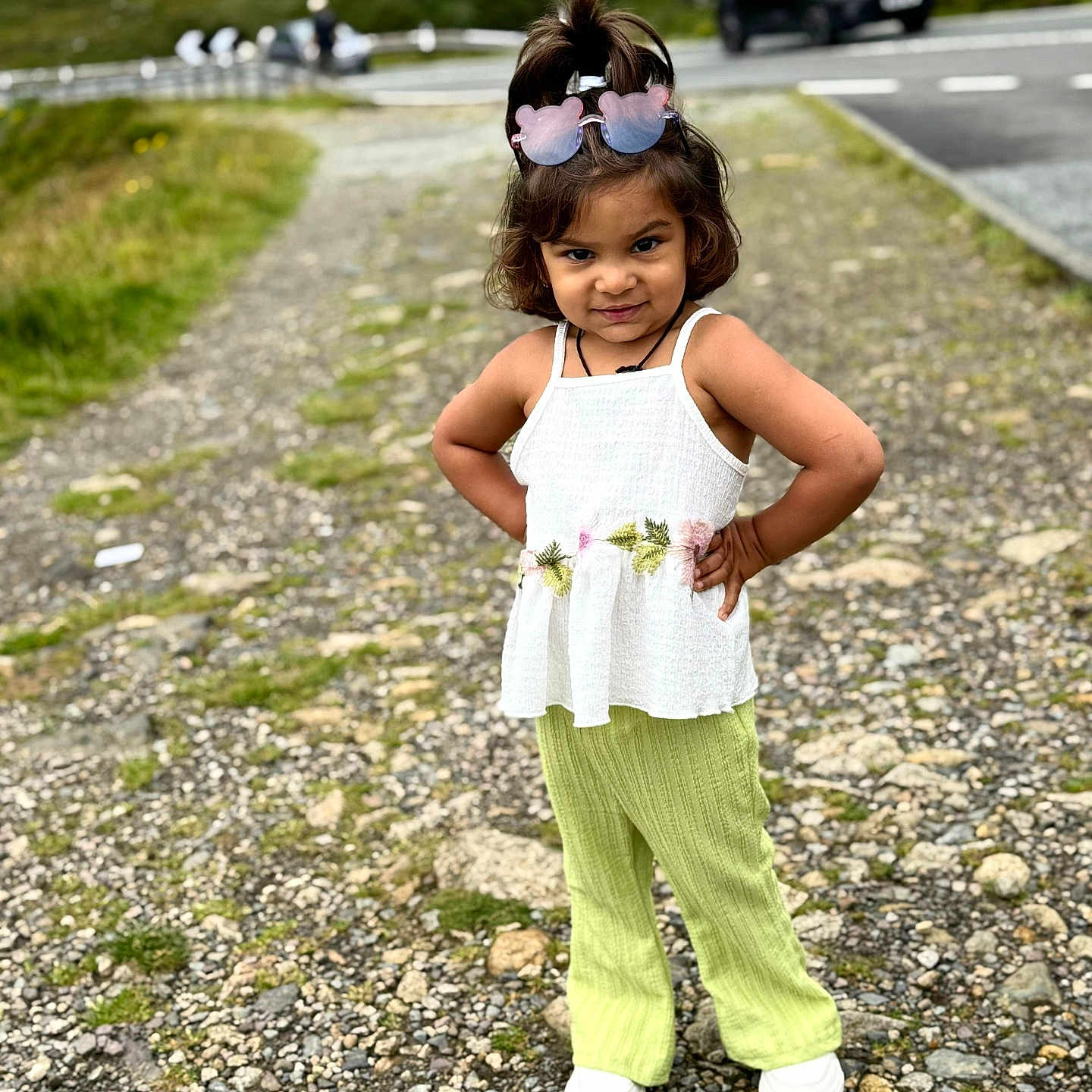Devanshi Patel is registered to the contest to win money with this photo: car, casual_clothing, child, confident, daylight, footwear, girl, green_pants, greenery, hair_tied, nature, outdoor, path, portrait, posing, road, rocks, standing, sunglasses, white_top