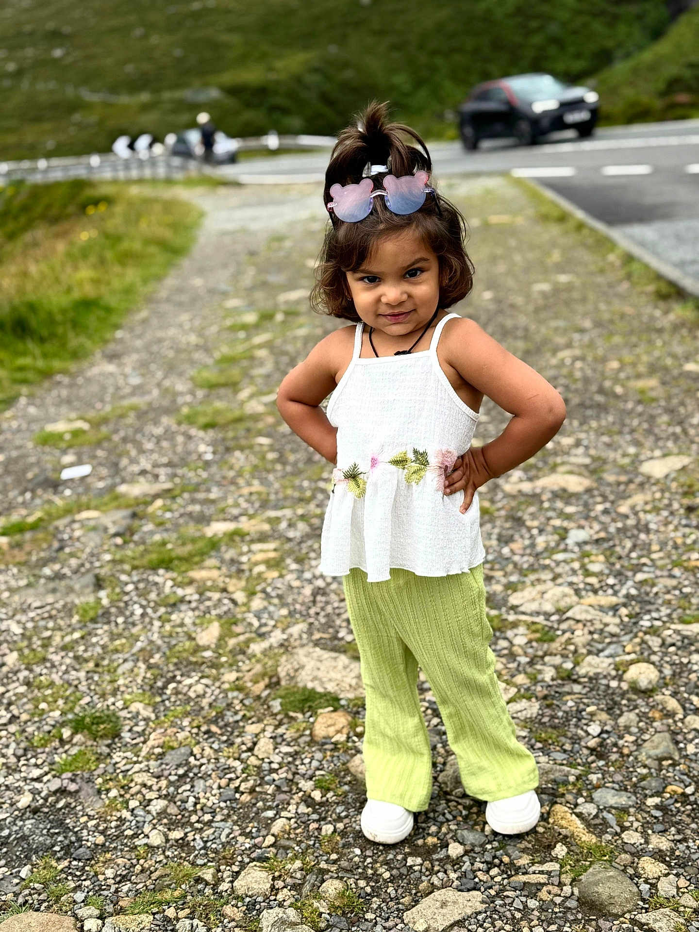 Devanshi Patel is registered to the contest to win money with this photo: child, girl, outdoor, path, rocks, greenery, road, car, sunglasses, white_top, green_pants, standing, posing, hair_tied, confident, footwear, nature, portrait, casual_clothing, daylight