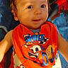 Timothy is registered to the contest to win money with this photo: baby, child, infant, portrait, smiling, sitting, indoors, face, eyes, hair, orange_bib, car_graphic, colorful_clothing, blanket, fabric, close_up, baby_clothing, happy, photography, race_car