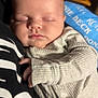 Ronnie is registered to the contest to win money with this photo: baby, blanket, closeup, clothing, comfort, cozy, face, hand, holding, indoor, infant, pajamas, peaceful, person, portrait, resting, sleeping, soft_lighting, text, young_child