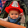 baby, child, firefighter_hat, red_hat, stroller, smile, face, blue_eyes, denim_overalls, cute, portrait, infant, clothing, seatbelt, baby_seat, indoor, person, happy, headwear, closeup