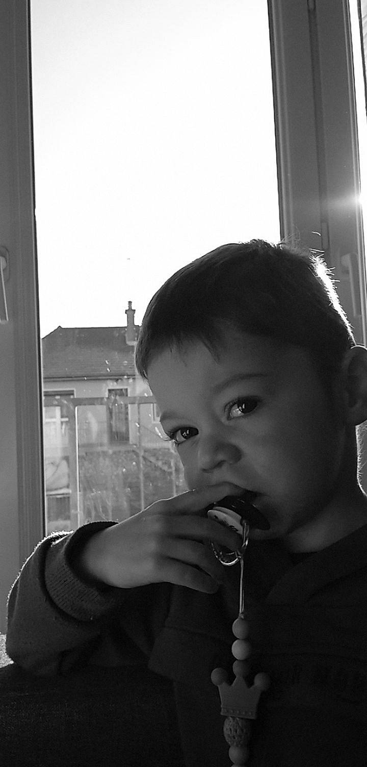 Noé participe au concours pour gagner de l'argent avec cette photo : black, black_and_white, child, curtain, fun, gesture, glass, hairstyle, happy, human, monochrome, monochrome_photography, person, standing, style, toddler, white, window