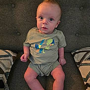 Karson is registered to the contest to win money with this photo: baby, child, toddler, sitting, couch, gray, hair, mohawk, dinosaur, clothing, patterned_pillows, indoors, cute, portrait, expression, legs, hands, furniture, casual, young
