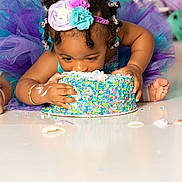 A'Myri is registered to the contest to win money with this photo: toddler, cake, sprinkles, tutu, headband, birthday, celebration, colorful, frosting, messy, happy, child, cute, indoors, footwear, bracelet, face, hands, sitting, playful