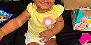 A'Myri joined the competition — help win amazing prizes! baby, child, smiling, sitting, yellow_shirt, white_socks, bows, hair_buns, diaper_box, car_seat, black_background, happy, indoor, cute, infant, clothing, person, toddler, toy, fabric