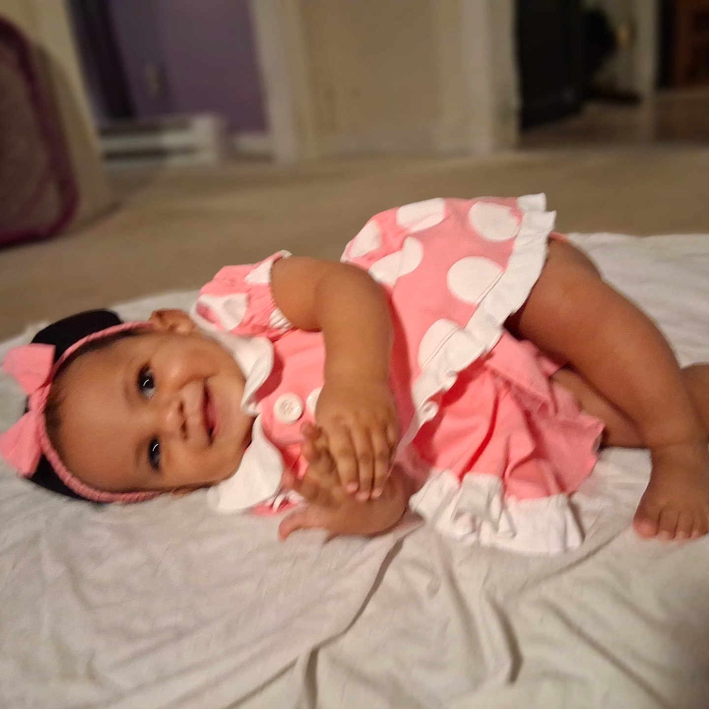 Malani joined the competition — help win amazing prizes! baby, child, infant, pink_dress, headband, smile, clapping, lying_down, white_sheet, indoors, floor, happy, cute, polka_dot, toddler, skin, face, hands, foot, playful