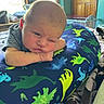 baby, infant, dinosaur_pillow, blanket, bedroom, window, wooden_door, striped_clothing, face, expression, indoor, resting, child, person, soft_light, cozy, toddler, skin, head, pose