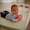 baby, child, toy, red_ball, striped_shirt, mat, floor, indoor, curious, blue_eyes, infant, playtime, soft_lighting, casual_clothing, crawling, young_child, blanket, home, cute, portrait