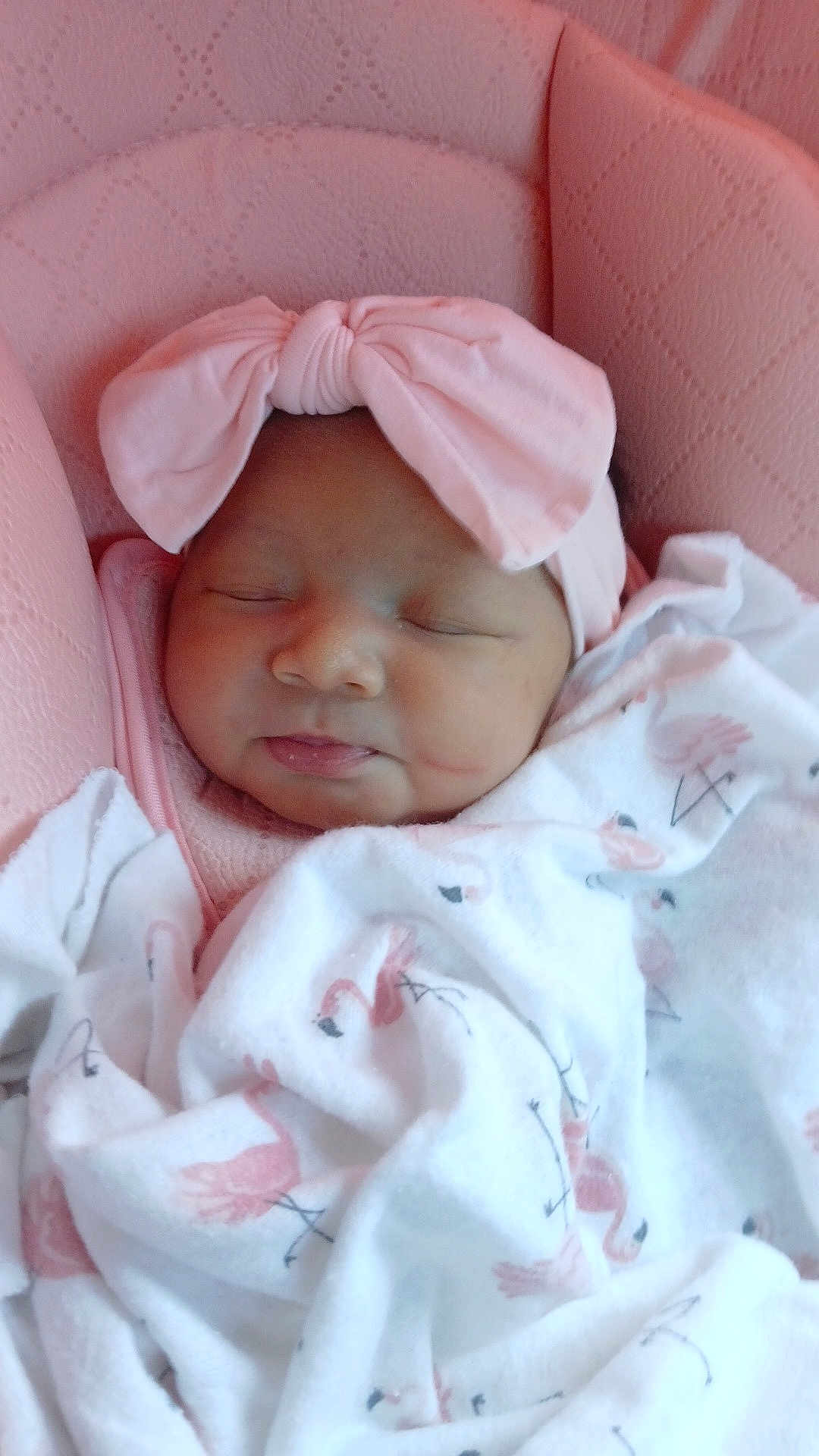 Amoura joined the competition — help win amazing prizes! baby, sleeping, blanket, flamingo_pattern, pink_bow, headband, cushioned_seat, soft_texture, infant, cozy, cute, portrait, child, resting, indoors, closeup, peaceful, newborn, wrapped, adorable