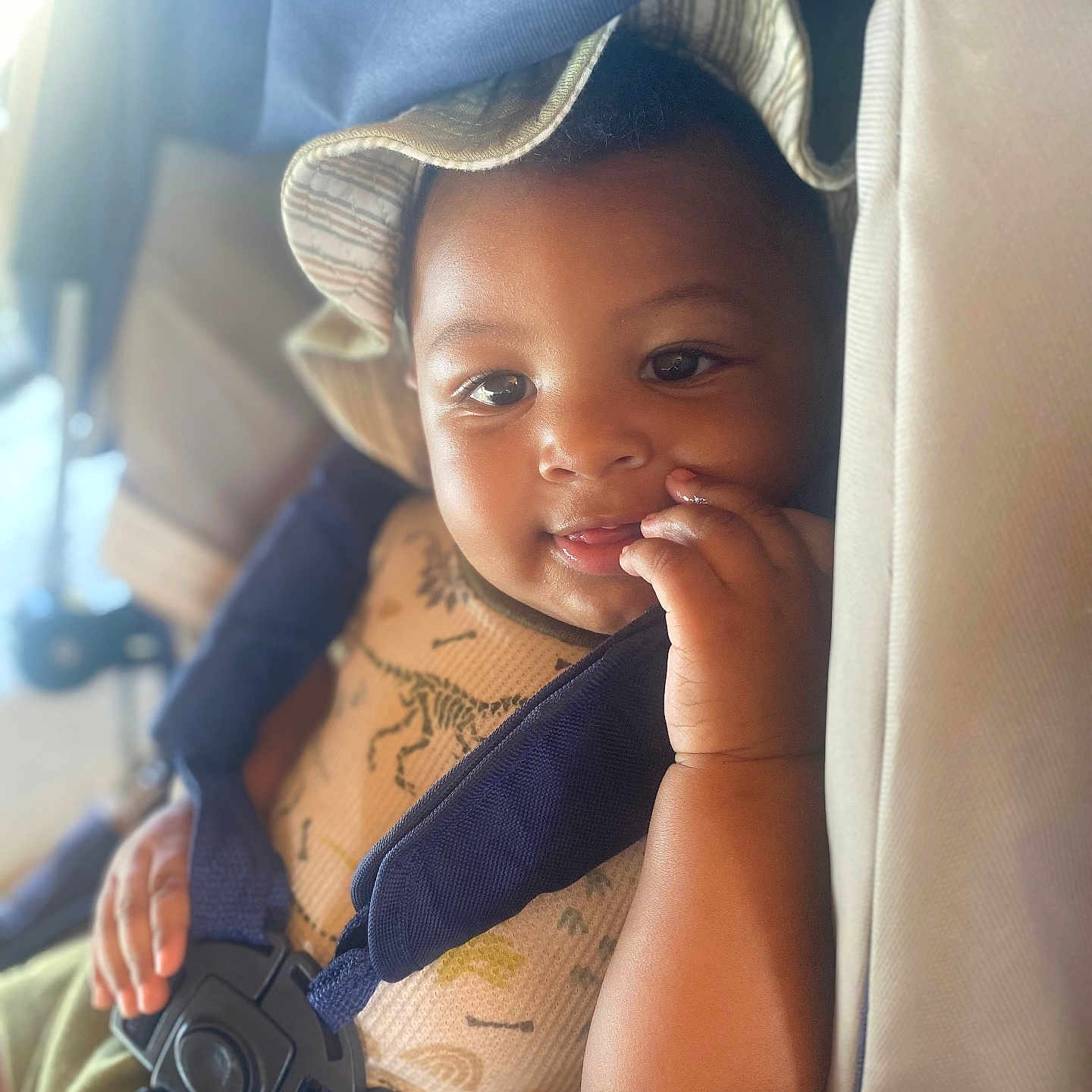 Zyair is registered to the contest to win money with this photo: child, toddler, baby, face, portrait, car_seat, seatbelt, hat, smiling, curious, finger, sitting, vehicle, travel, indoors, close_up, brown_skin, clothing, passenger, safe
