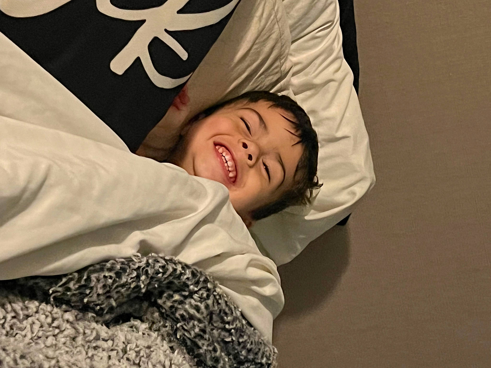 Grayson is registered to the contest to win money with this photo: bedding, child, comfort, eye, flash_photography, font, fun, fur, gesture, happy, joy, linens, logo, monochrome_photography, person, portrait_photography, room, sitting, sleep, sleeve