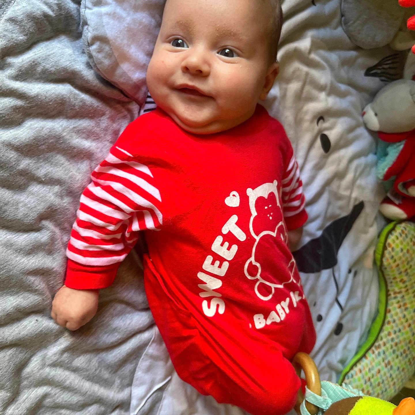 Séolan participe au concours pour gagner de l'argent avec cette photo : baby, bird_toy, blanket, child, cute, fabric_toy, face, happy, head, indoors, infant, lying_down, person, playful, quilted, red_clothing, smiling, soft_toys, striped_sleeves, young_child