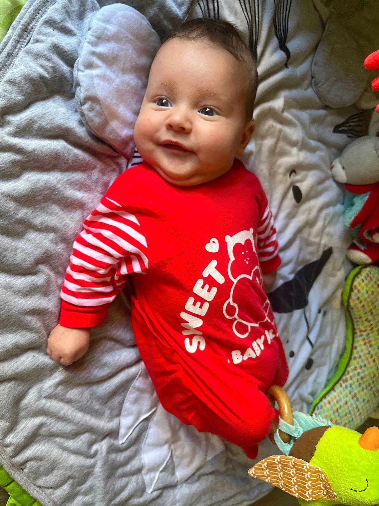 Séolan participe au concours pour gagner de l'argent avec cette photo : baby, infant, red_clothing, striped_sleeves, smiling, lying_down, blanket, quilted, soft_toys, bird_toy, fabric_toy, cute, child, indoors, playful, happy, face, head, person, young_child