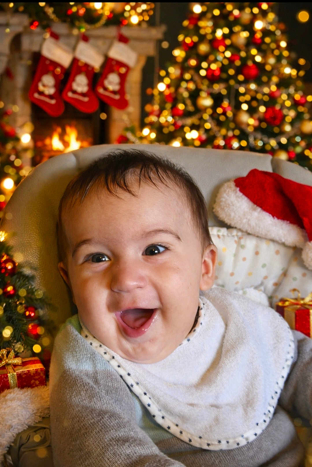 Timéo participe au concours pour gagner de l'argent avec cette photo : baby, bib, celebration, child, christmas_tree, cozy, decorations, face, festive, fireplace, gift, happy, holiday, indoor, infant, santa_hat, seat, smiling, stockings, warmth