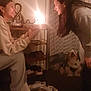 two_people, smiling, birthday_cake, lit_candles, dog, slippers, shoes, socks, indoor, curtain, shelf, warm_lighting, candid, friends, celebration, pet, sitting, cozy, low_light, portrait