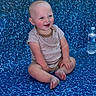 baby, child, smiling, sitting, onesie, blue_eyes, water_bottle, patterned_surface, happy, cute, infant, barefoot, rosy_cheeks, short_hair, indoor, playful, portrait, person, young, casual