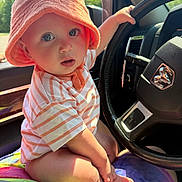 Duston joined the competition — help win amazing prizes! baby, child, orange_hat, striped_shirt, car_interior, steering_wheel, colorful_blanket, curious, wide_eyes, sitting, hand_on_wheel, sunlight, window, dashboard, cute, infant, portrait, closeup, indoors, seat