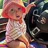 baby, child, orange_hat, striped_shirt, car_interior, steering_wheel, colorful_blanket, curious, wide_eyes, sitting, hand_on_wheel, sunlight, window, dashboard, cute, infant, portrait, closeup, indoors, seat