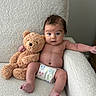 baby, teddy_bear, diaper, chair, couch, plush_toy, infant, skin, expression, person, cute, indoor, white, comfort, soft_texture, child, portrait, relaxing, seated, toy
