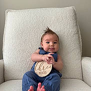 Coast is registered to the contest to win money with this photo: baby, infant, three_months, blue_clothing, armchair, white_fabric, sign, wooden_sign, mohawk_hairstyle, cute, portrait, sitting, bare_feet, indoor, child, young_baby, smiling, hands, feet, person