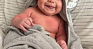 Coast is registered to the contest to win money with this photo: animal_ears, baby, blanket, child, cozy, cute, happy, hood, indoors, infant, lying_down, person, portrait, skin, smile, soft_texture, striped_blanket, towel, wrapped, young