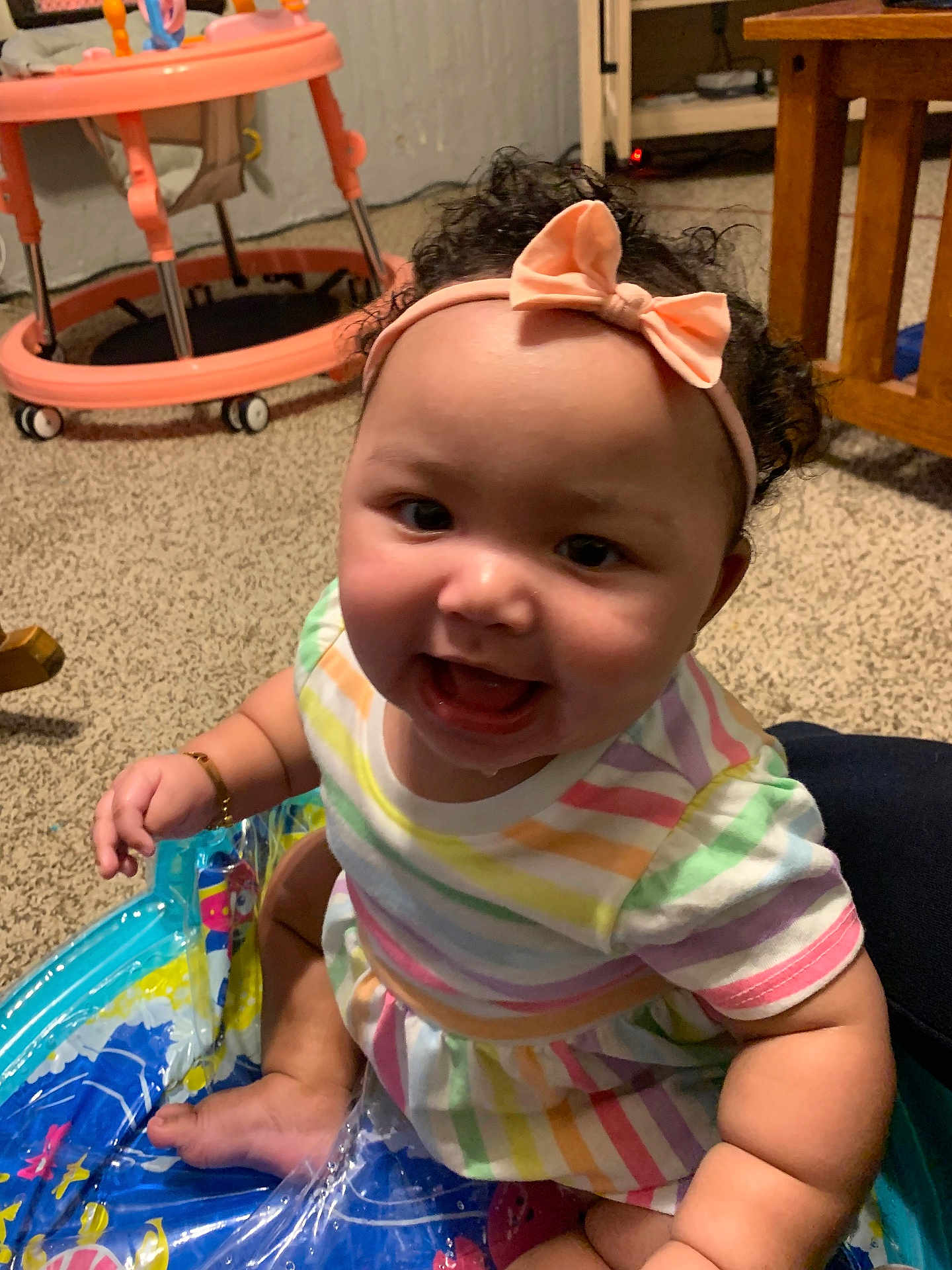 Jaiyanna joined the competition — help win amazing prizes! baby, child, infant, headband, bow, striped_dress, colorful_clothing, drool, indoor, carpet, baby_walker, wooden_furniture, playful, inflatable_pool, happy, smiling, curly_hair, person, cute, sitting