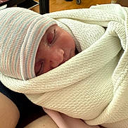 Ravi joined the competition — help win amazing prizes! newborn, baby, sleeping, blanket, hat, hospital_room, medical_equipment, wooden_floor, person, infant, wrapped, closeup, peaceful, resting, human_skin, soft_texture, indoors, parent, holding, tired