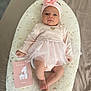 baby, infant, pink_clothing, headband, flower, tutu, milestone_card, cute, lying_down, cushion, soft_texture, one_month, celebration, indoors, child, portrait, small_feet, hand, face, curious