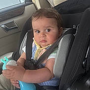 Liam joined the competition — help win amazing prizes! baby, child, car_seat, toy, car_interior, seatbelt, infant, person, holding, clothing, striped_pants, colorful_shirt, safety, seat, cute, closeup, indoor, baby_toy, young_child, car_window
