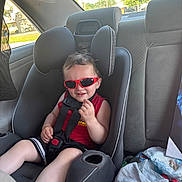 Nathaniel is registered to the contest to win money with this photo: toddler, child, car_seat, sunglasses, red, seatbelt, car_interior, window, sunlight, smile, shorts, clothing, seat, safety, person, happy, casual, hair, skin, daylight