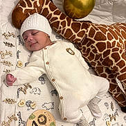 Kazadi a rejoint le concours — aidez-le/la à gagner de superbes lots ! animal_print, baby, balloon, blanket, cozy, cute, decor, infant, knit_hat, knit_onesie, lying_down, milestone, nursery, peaceful, plush_giraffe, sleeping, smiling, soft_toy, striped_socks, wooden_sign